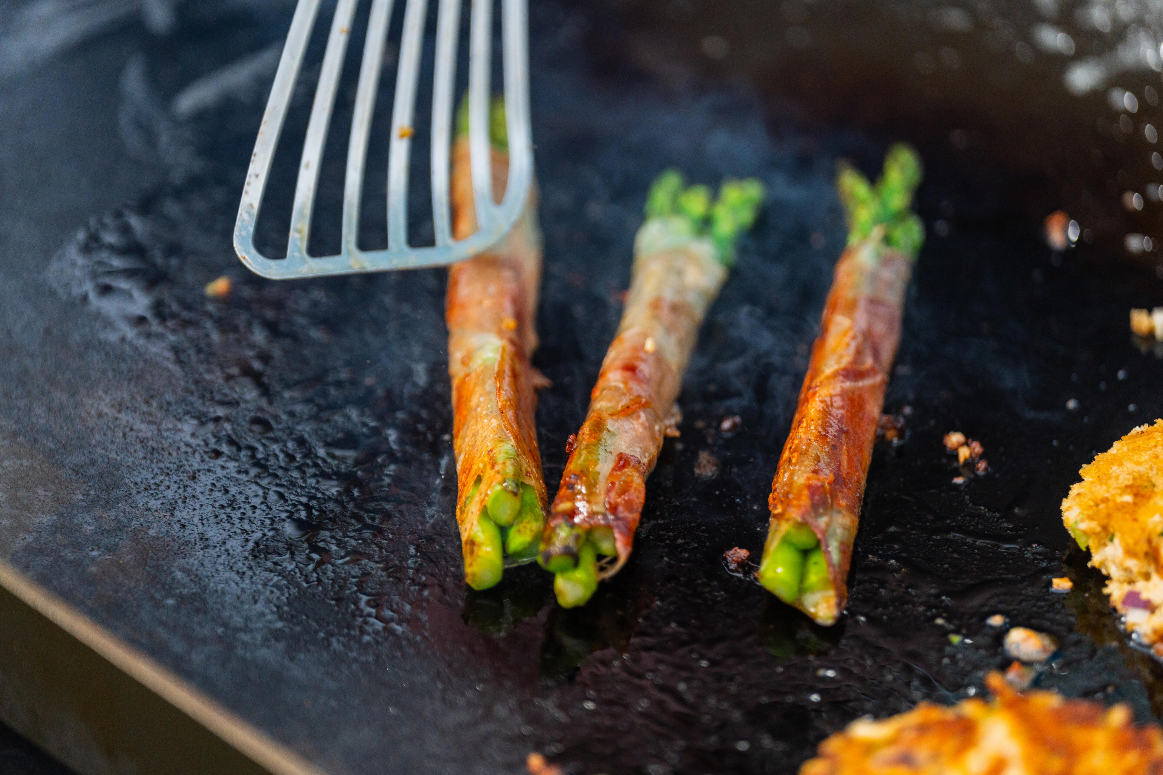 Asparagus spears searing on a hot griddle with a spatula, garnished with seasonings
