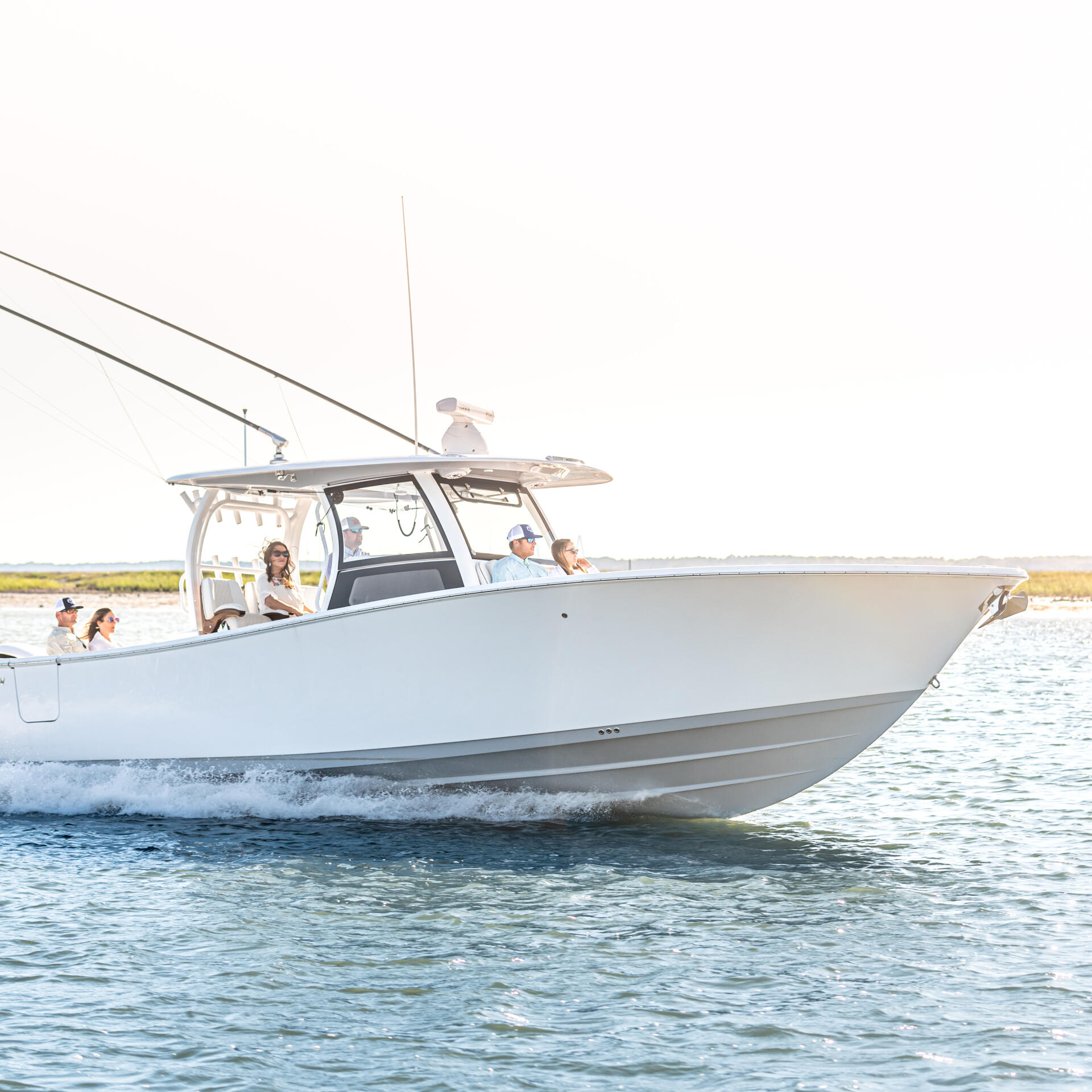 White center console boat with hard-top running through shallow coastal water with passengers aboard