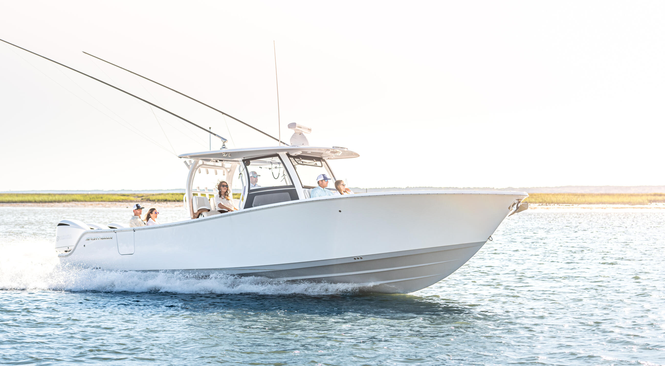 White center console boat with hard-top running through shallow coastal water with passengers aboard