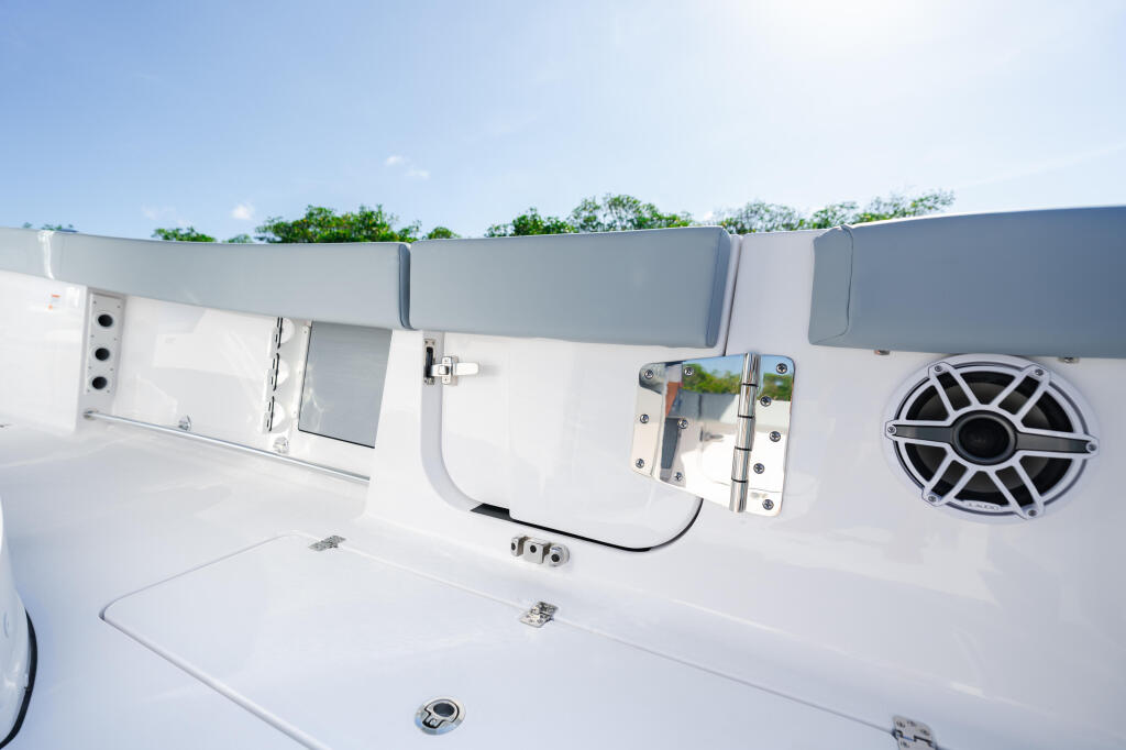 White boat gunwale with gray cushioned seating, equipment mounted on rails, and speaker system visible against blue sky