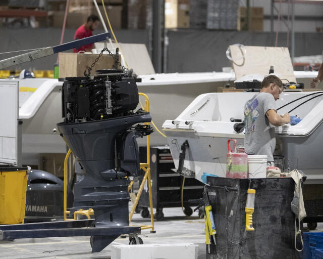 Yamaha outboard engine being hoisted in a boat manufacturing facility with workers assembling nearby vessels